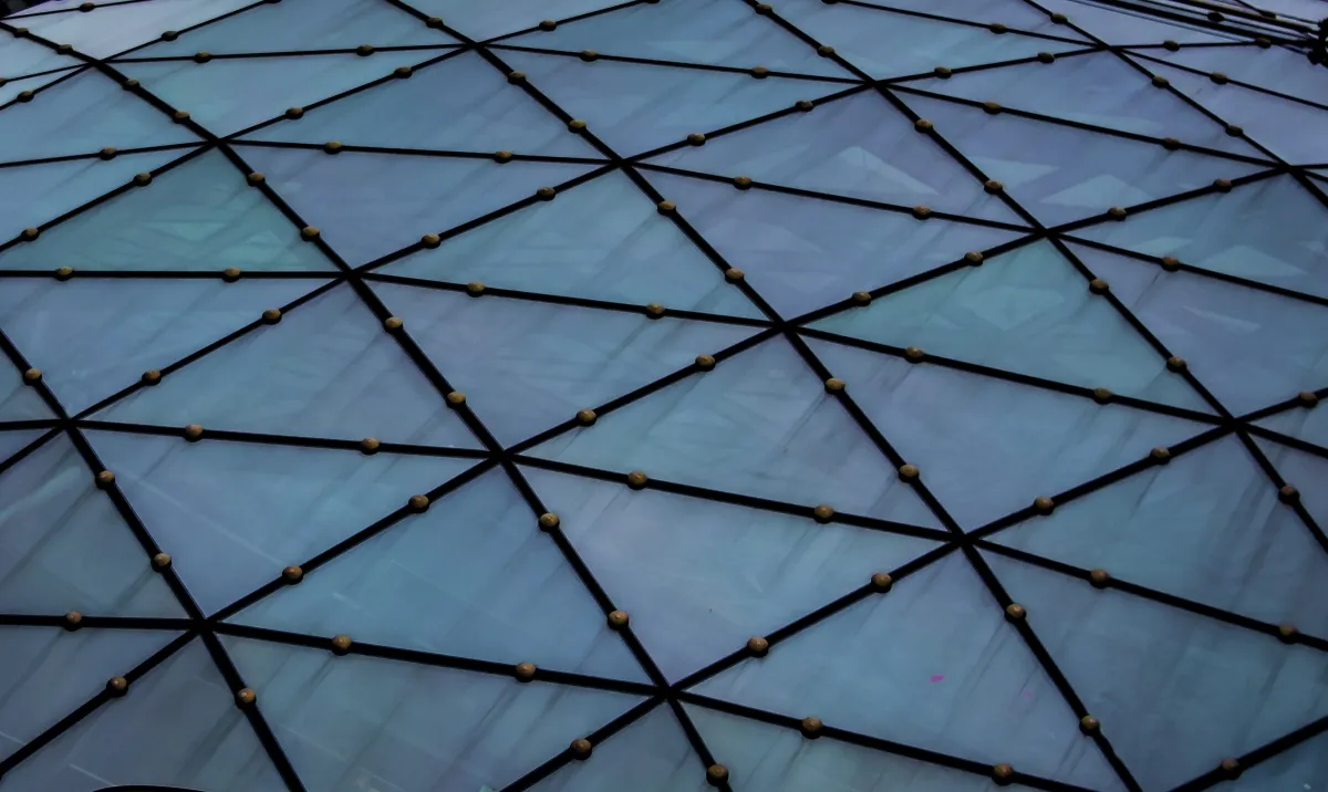 Blue-tinted triangular glass facade patterned with black lines and brass nodes